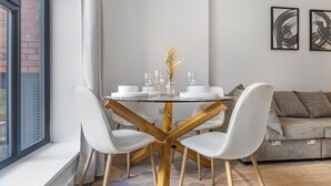 A modern dining area with a glass table, white chairs, and a vase with dried plants.