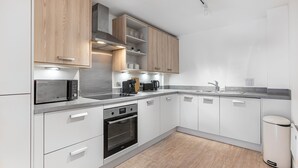 A modern kitchen with white cabinets, a built-in oven, a microwave, a coffee maker, and a sink.