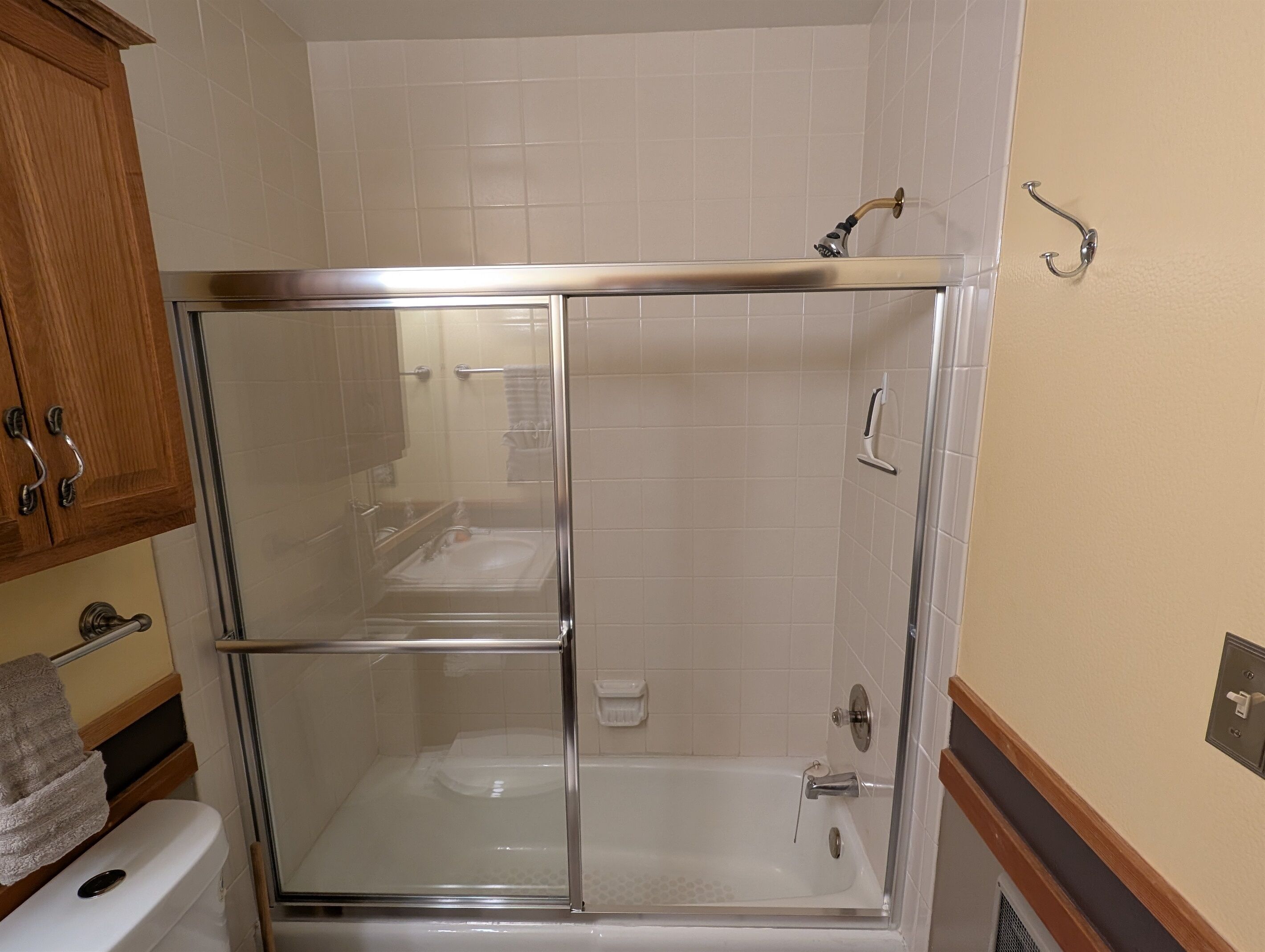 A glass-enclosed shower with a bathtub, wooden cabinets, and a towel rack.
