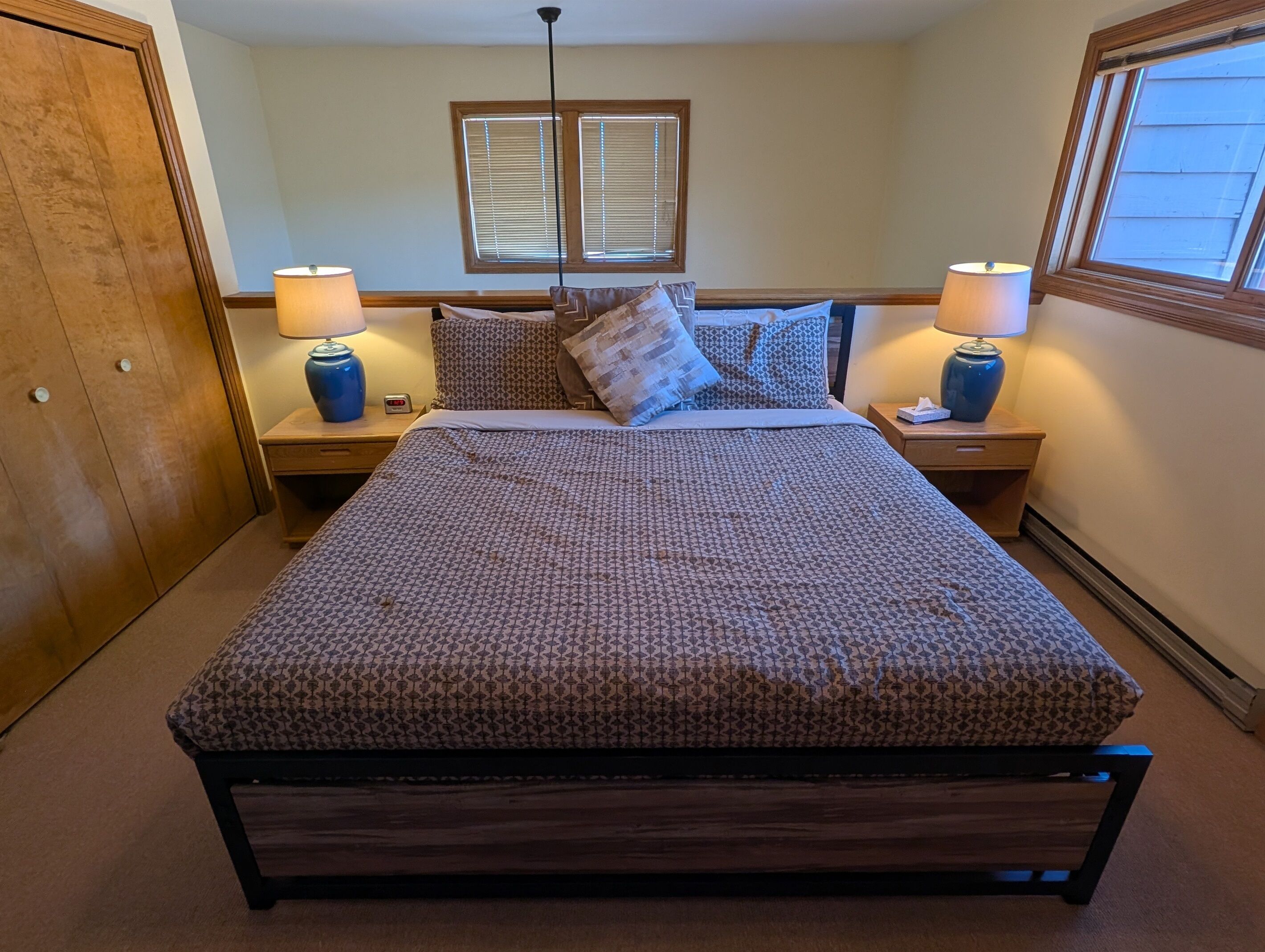 A neatly made bed with patterned bedding, two bedside lamps, and a window with blinds.
