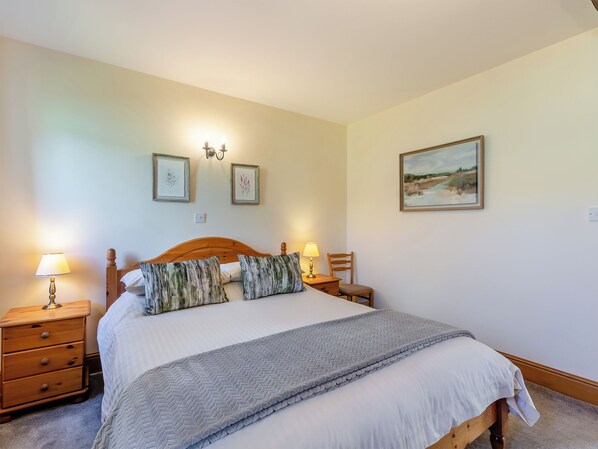 Un dormitorio ordenado con una cama de madera, dos mesitas de noche con lámparas, una mesita auxiliar y un cuadro en la pared.