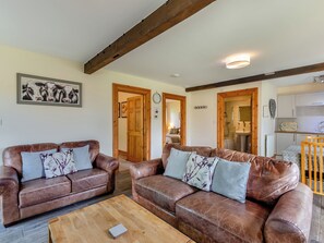 Ein Wohnzimmer mit zwei braunen Ledersofas, einem Holztisch und einer Küchenzeile mit weißen Schränken und einer Spüle.