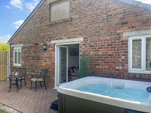 A brick house with a patio, a hot tub, and a door leading to a room.