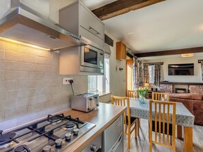 Une cuisine moderne équipée d’une cuisinière à gaz, d’un four à micro-ondes et d’un grille-pain. On y trouve un coin repas avec une table et des chaises, ainsi qu’un canapé à l’arrière-plan.