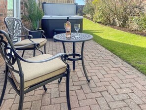Une terrasse extérieure avec deux chaises en métal et une table, une bouteille de vin et un jacuzzi.