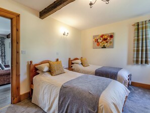 A bedroom with two beds, wooden headboards, a painting on the wall, and a window with curtains.