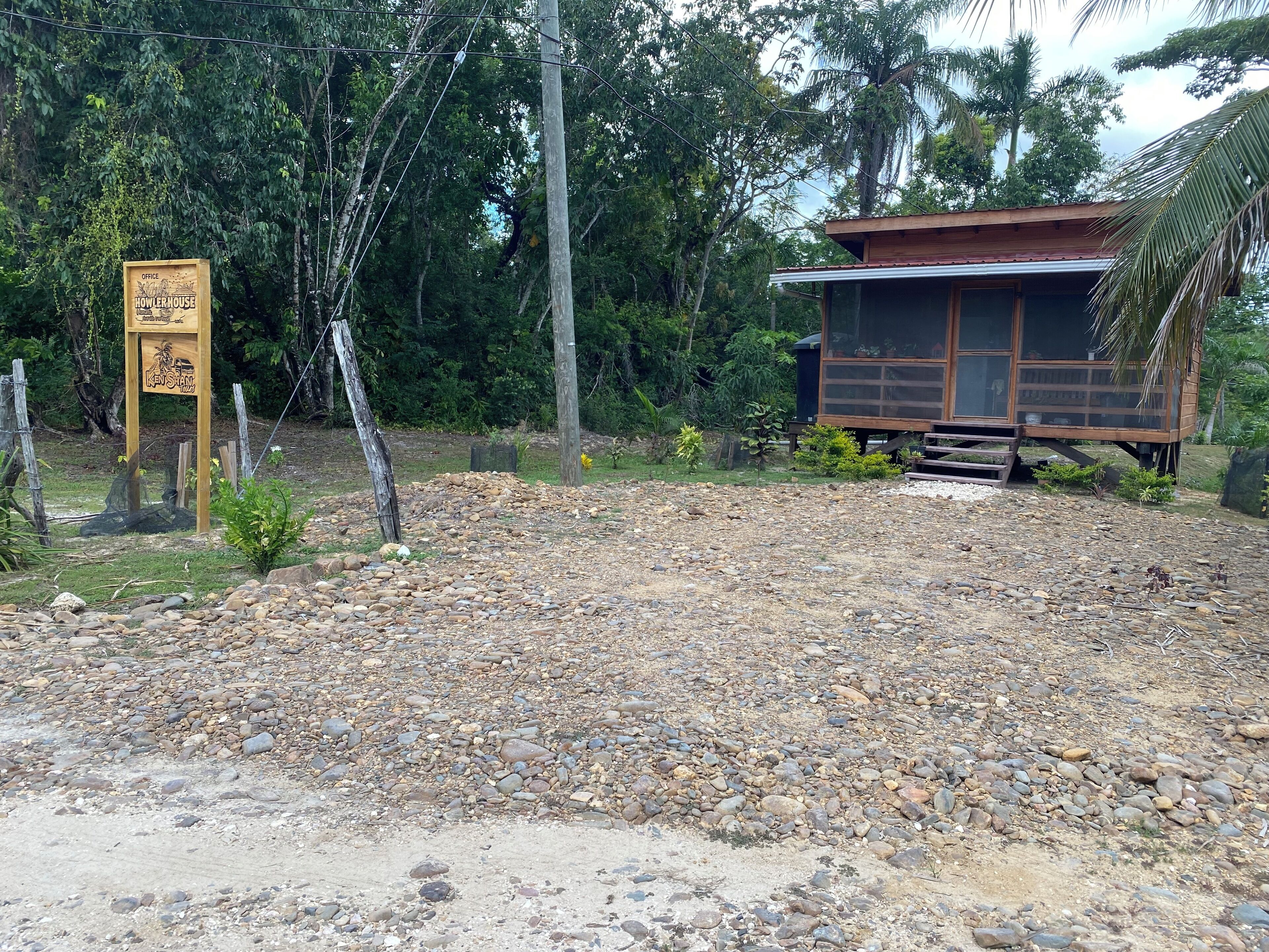 A rustic wooden structure with a gravel path leading to it, surrounded by dense greenery.