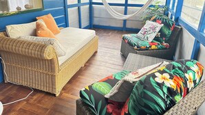 Una habitación con un sofá de mimbre, un banco acolchado y una hamaca.