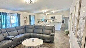 A modern living room with a sectional sofa, a round coffee table, and a kitchen in the background. - Refuge by Southern Oaks. Charming 3 bed 2 bath. Very close to Lake Murray! (Gilbert)