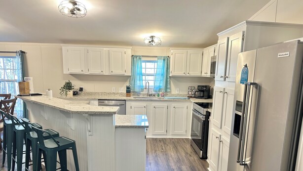 A modern kitchen with white cabinetry, a central island with bar stools, a stainless steel refrigerator, and a built-in oven. - Refuge by Southern Oaks. Charming 3 bed 2 bath. Very close to Lake Murray! (Gilbert)