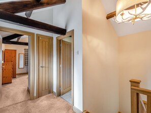 Un pasillo con puertas de madera, una escalera con barandilla de madera y un candelabro en el techo.