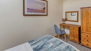 Ein Schlafzimmer mit einem Bett, einem Schreibtisch, einem Stuhl, einem Kleiderschrank und einem gerahmten Bild an der Wand.