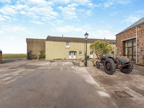 Un edificio con camino de entrada pavimentado, un tractor estacionado y un muro de piedra.