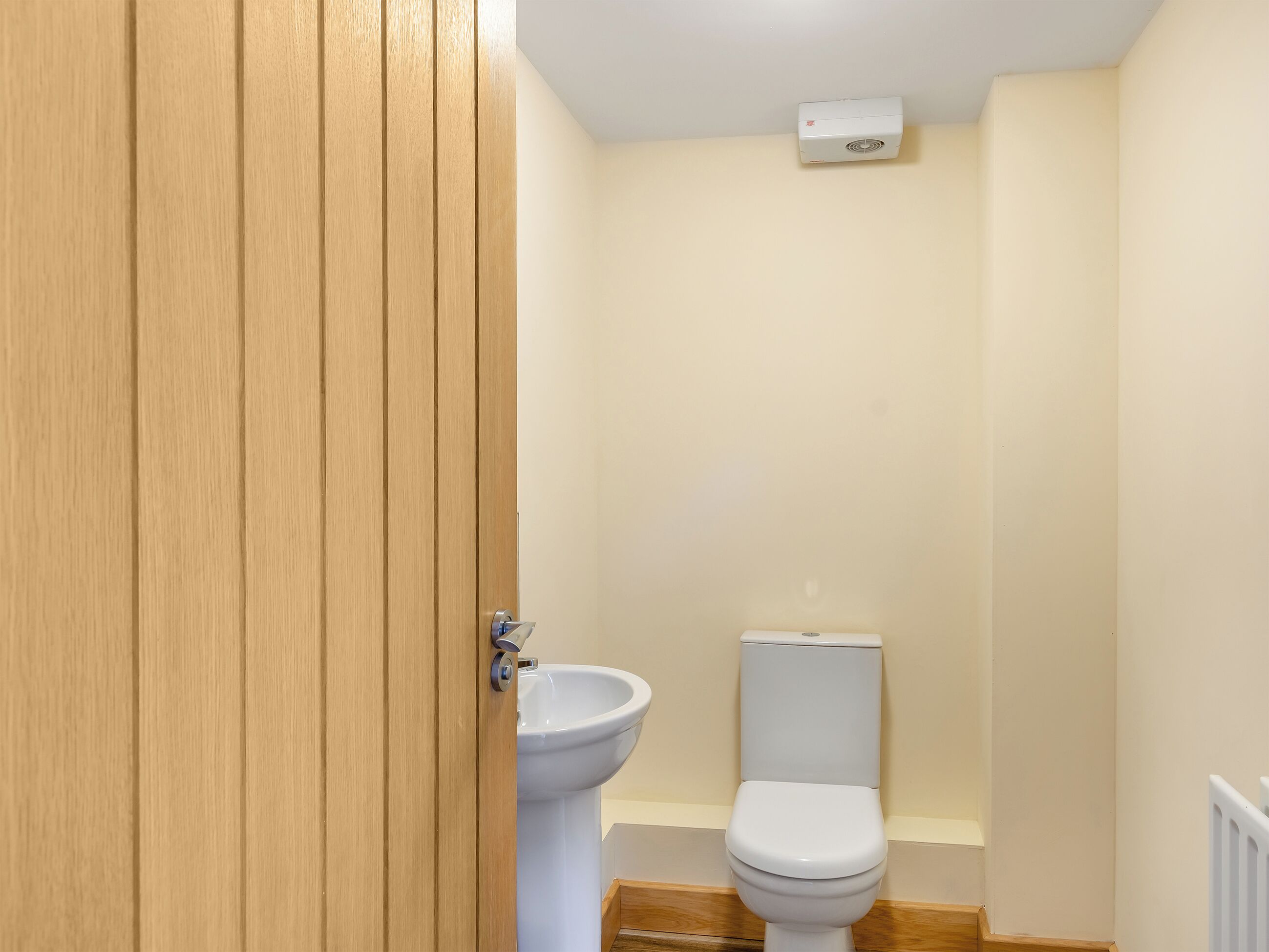 Une petite salle de bain propre, avec une porte en bois, des toilettes blanches et un lavabo blanc.