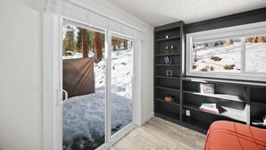 Habitació amb una porta corredissa de vidre que dona a una zona exterior nevada, una estanteria amb diversos objectes i una finestra amb vista a l'exterior.