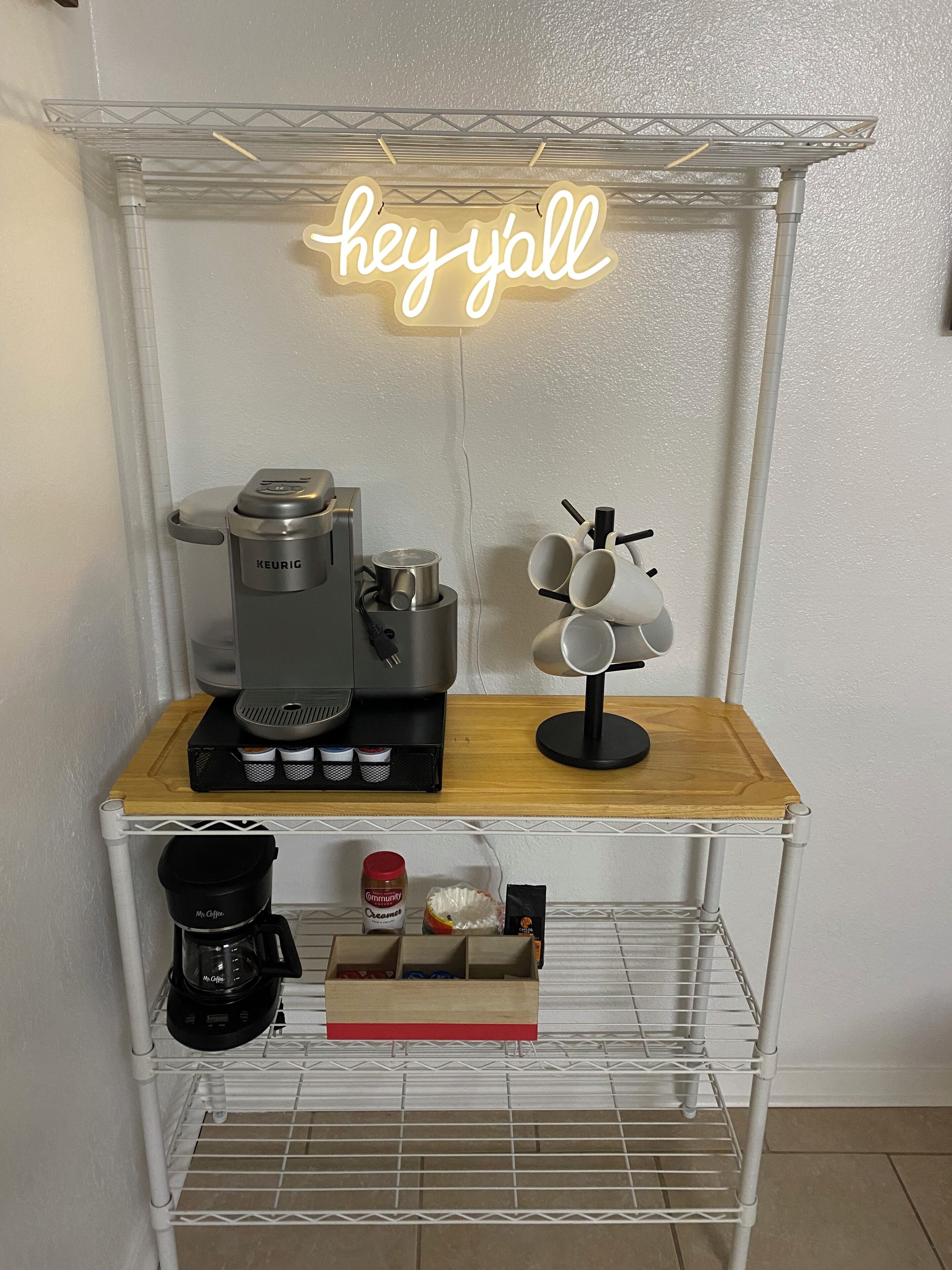 Une petite cuisine équipée d’une machine à café, d’un porte-tasses et d’un néon.