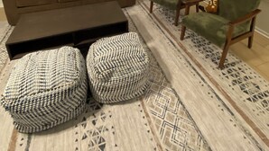 Una sala de estar con un sofá marrón, dos otomanas, una mesa de centro y una alfombra estampada.