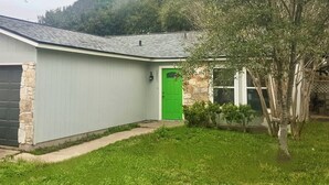 Una casa de un piso con garaje, una puerta verde y un muro de piedra decorativo.