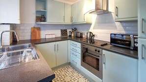 A modern kitchen with light blue cabinets, a stainless steel sink, and a built-in oven. - Shoreline Angel Apartments (South Shields)