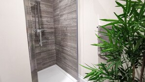 A shower with a glass door, tiled walls, and a bamboo plant beside it. - Shoreline Angel Apartments (South Shields)