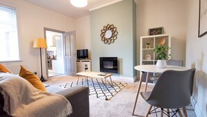 A modern living room with a sofa, a coffee table, a TV, and a fireplace. - Shoreline Angel Apartments (South Shields)