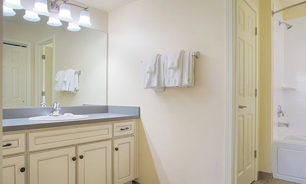 A bathroom with a sink, mirror, towel rack, and a shower area.