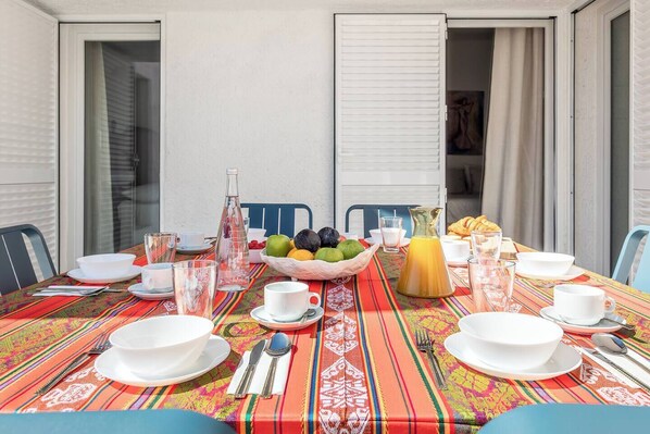 A dining table set with white plates, bowls, and glasses, a pitcher of orange juice, and a fruit bowl with various fruits.