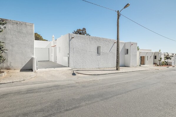 Une rue tranquille, bordée de bâtiments blancs, avec un ciel dégagé et un lampadaire.