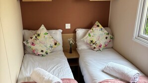 A twin room with two beds, each with a pink bedspread and floral pillows. There is a wooden shelf above the beds with a 'love' sign. - Beautiful Caravan Phoenix In St Margaret's Bay. Pet Friendly (Saint Margaret's at Cliffe)
