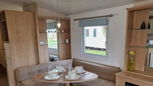 A compact kitchen with a dining area, including a round table set for four, a built-in bench, and a small window. - Beautiful Caravan Phoenix In St Margaret's Bay. Pet Friendly (Saint Margaret's at Cliffe)