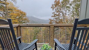 A wooden deck with two black chairs and a small table with a potted plant.