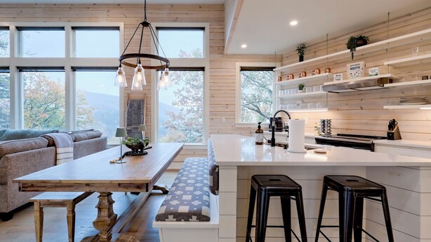 A modern kitchen with a large island, bar stools, and a view of the outdoors through large windows.