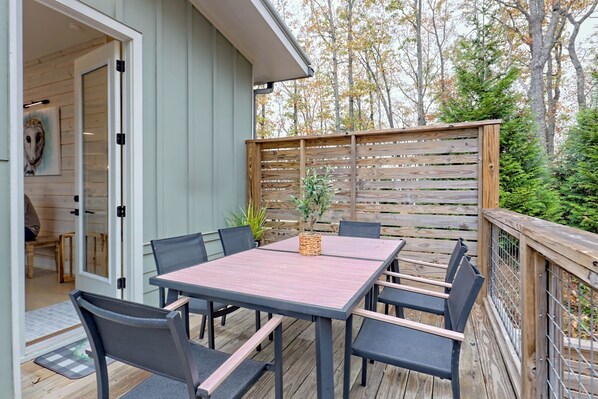 Una terraza de madera con una mesa y sillas, una valla de madera y una puerta que da a un espacio interior.
