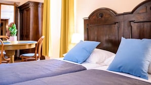 Una habitación de hotel con una cama grande, dos almohadas, un cabecero de madera, una mesita de noche con una lámpara y una silla.