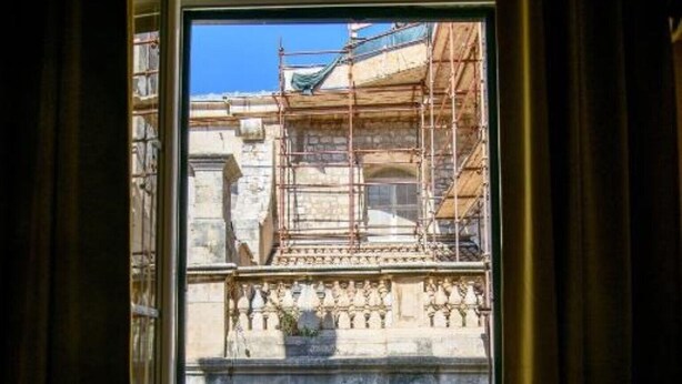 Vista a través de una ventana con cortinas, que muestra un edificio con andamios y fachada de piedra.