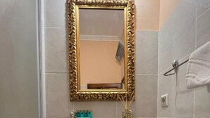 Ein Badezimmer mit einem weißen Waschbecken, einem spiegel mit goldener Rahmung und einem Handtuchhalter.
