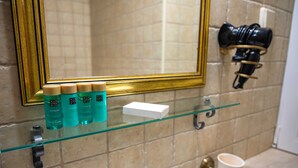 Un baño con un estante de vidrio que contiene artículos de aseo, un espejo y un perchero.