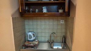 Una cocina compacta con un lavaplatos integrado, un refrigerador pequeño y una repisa sobre el lavaplatos con vajilla y utensilios de cocina.