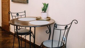 A dining area with a round table, two chairs, a potted plant, and framed pictures on the wall.
