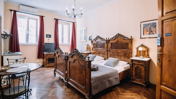 A bedroom with a wooden bed, a desk, a chair, a chandelier, and a television.