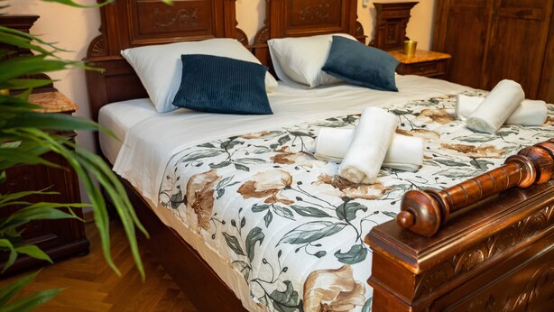 Una cama bien hecha con ropa de cama floral, un cabecero de madera y una mesita de noche con una lámpara.
