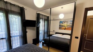 Un dormitorio con cama, espejo, televisor y un cuadro en la pared.