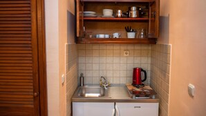 Una cocina compacta con un lavamanos empotrado, un refrigerador pequeño y un estante de madera sobre la encimera.