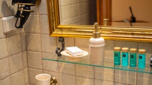 Un baño con espejo, secador de pelo, jabonera y varias botellas de champú y acondicionador.