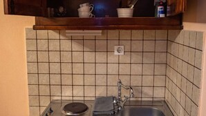 A compact kitchen with a built-in stove, a sink, and a wooden shelf above holding dishes and cookware.