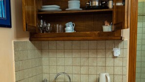 Une petite cuisine équipée d’un évier, d’une machine à café et d’un placard au-dessus de l’évier contenant de la vaisselle et des verres.