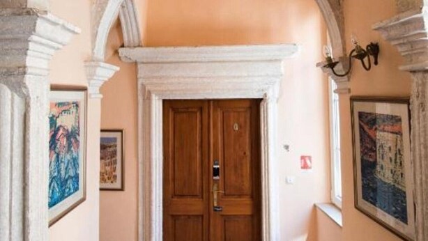 An arched hallway with a wooden door, stone steps, and framed artwork on the walls.