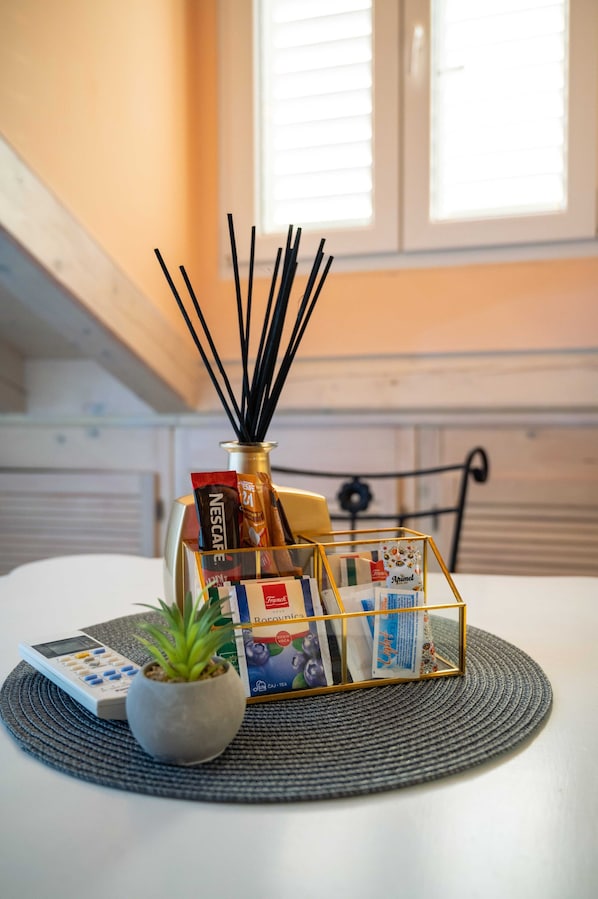 A table with a small potted plant, a white electronic device, and a decorative container holding various items including a box of Nescafe and a box of Cey Tea.