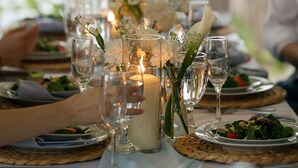 Ein gedeckter Tisch für eine Mahlzeit, mit Kerzen, Gläsern und einer Vase mit Blumen.