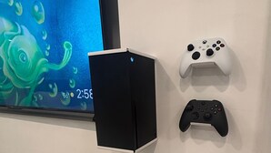 Eine schwarze Xbox Konsole und ein weißer Xbox Controller an einer weißen Wand angebracht.